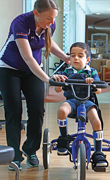 At Kennedy Krieger’s outpatient center, physical therapist Brittany Hornby helps Karam ride a tricycle.