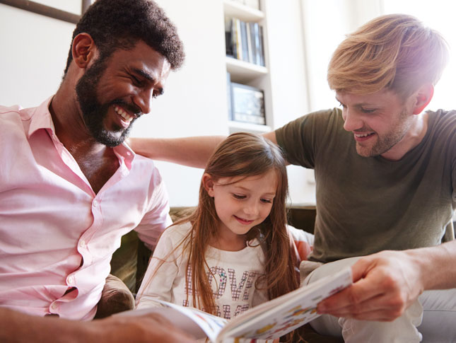 Male couple reads a book to their daughter.