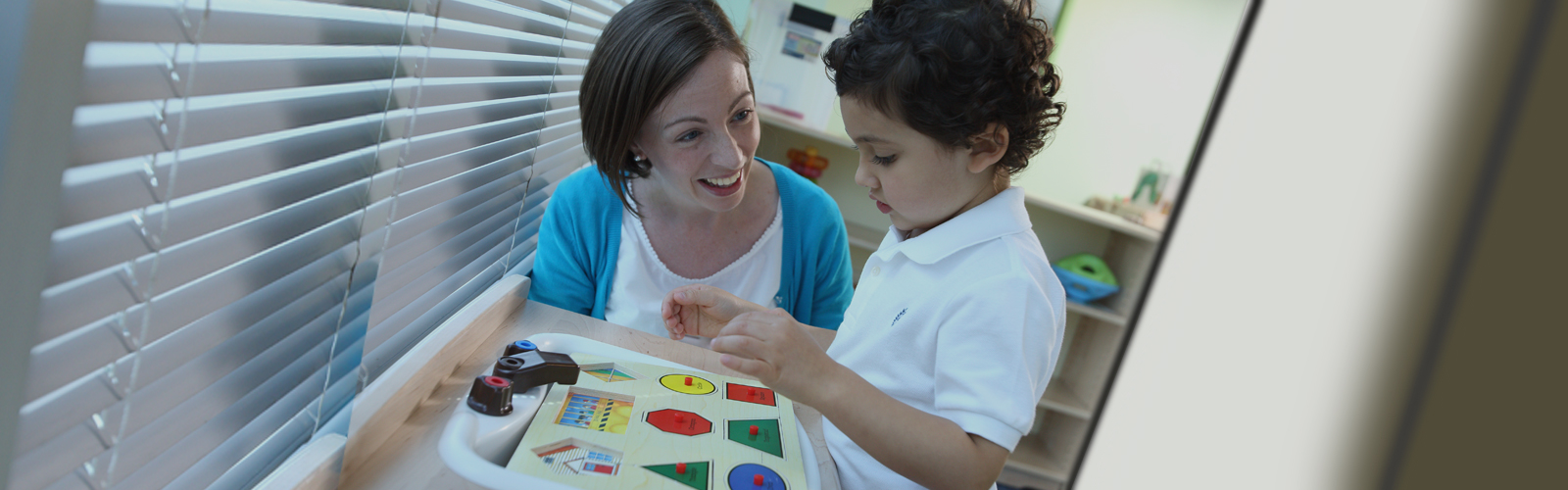 A child playing with a toy while an adult watches him and smiles.