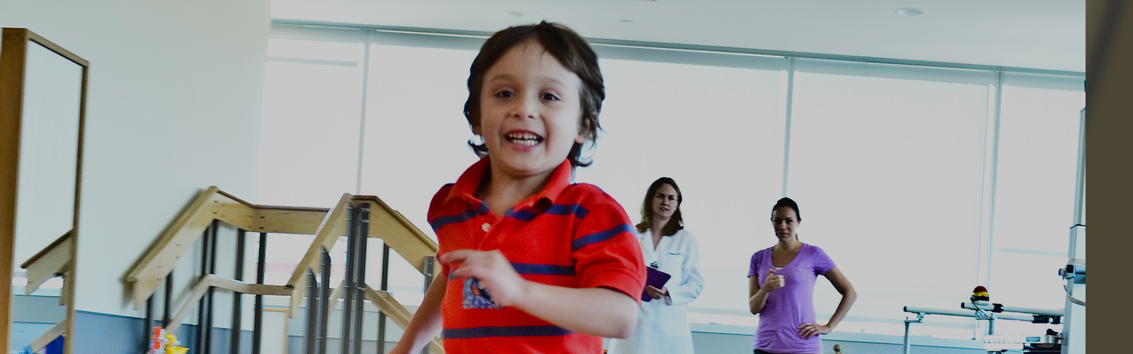 A child running and smiling with doctors watching in the background.