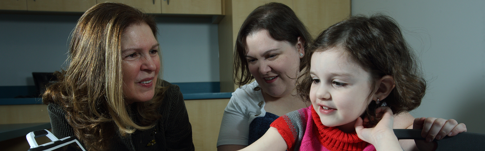 Dr. Landa sits with a patient and her mother as she reads a book