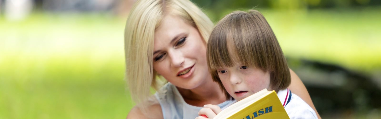 Young boy sitting on woman's lap reading book.