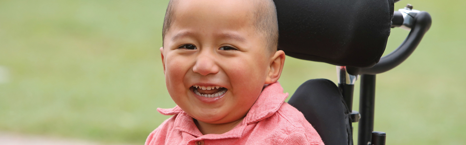 A young boy sitting in a wheelchair smiles.