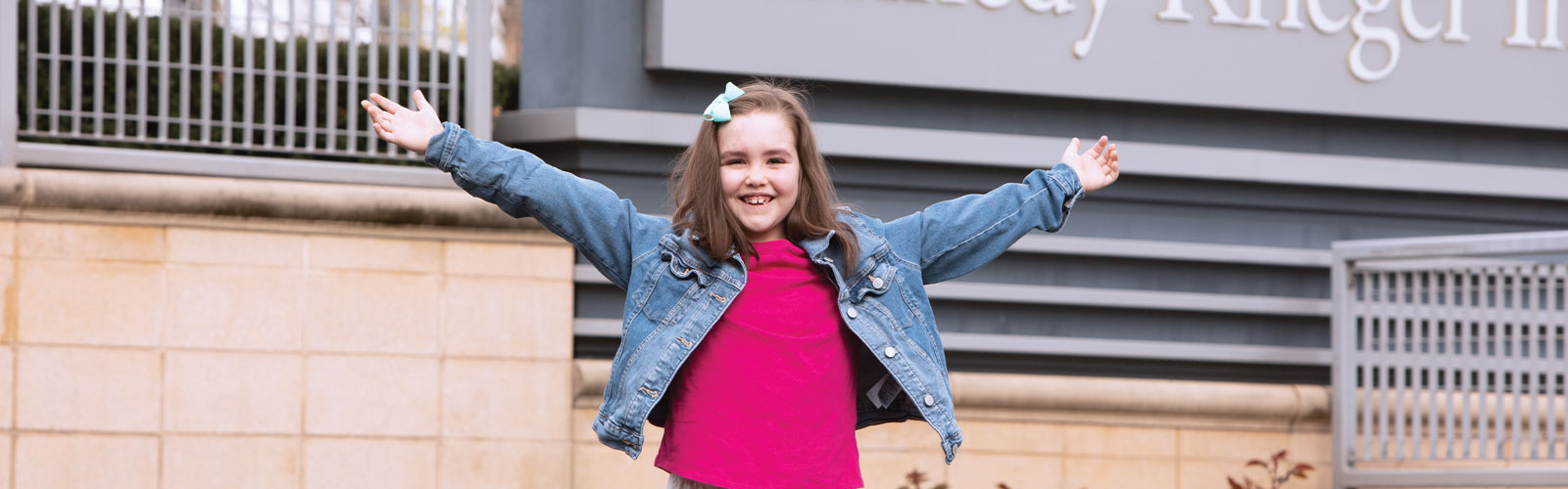 A young girl smiles with her arms outstretched. She has faint port wine-colored birthmarks across her forehead.