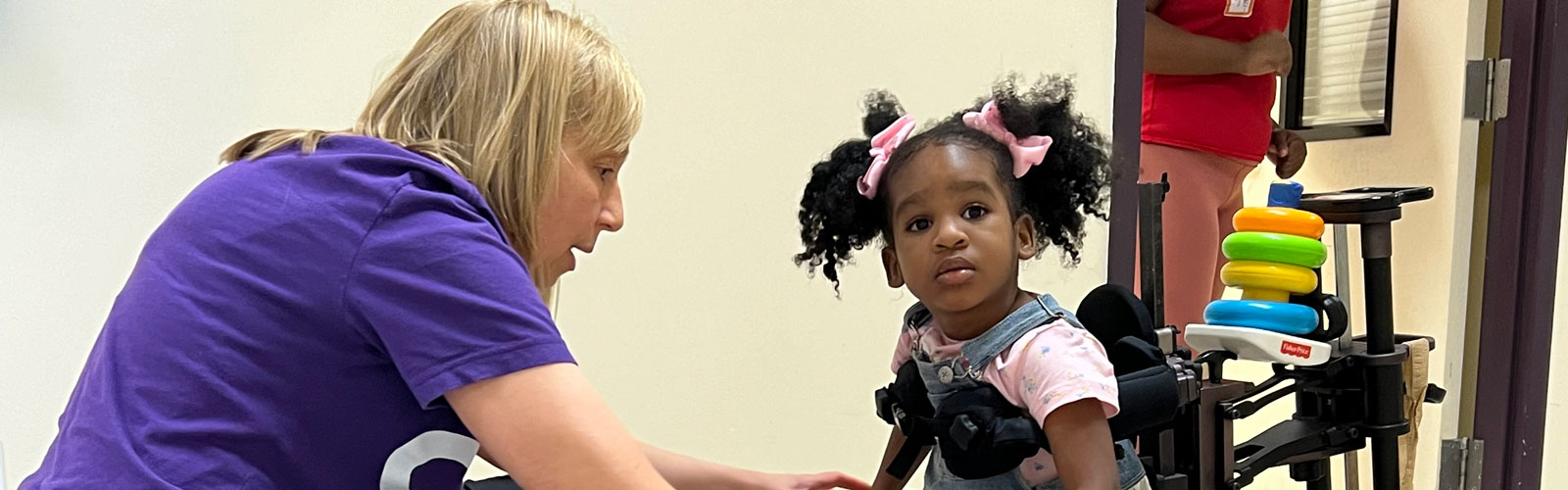 A physical therapist assists a little girl who is using a mobility device.