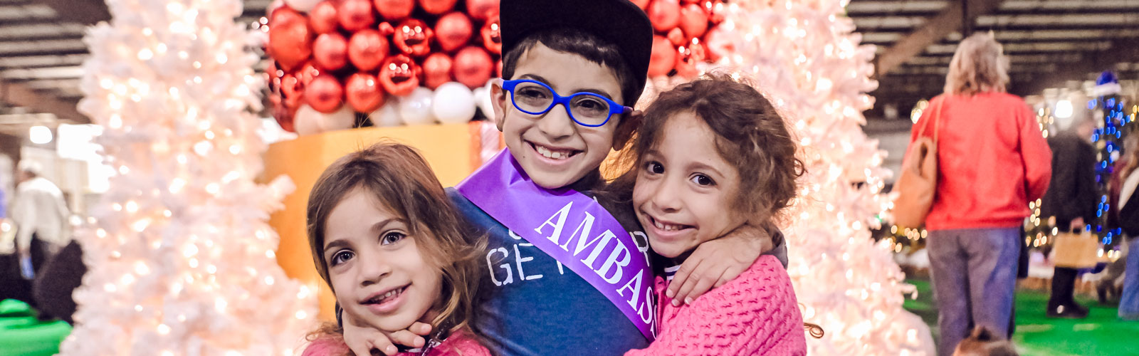 A Kennedy Krieger ambassador and his sisters smile at Festival of Trees.
