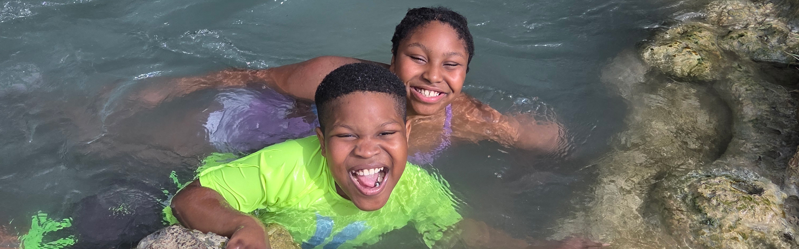 A Kennedy Krieger ambassador and his sister smile while swimming.