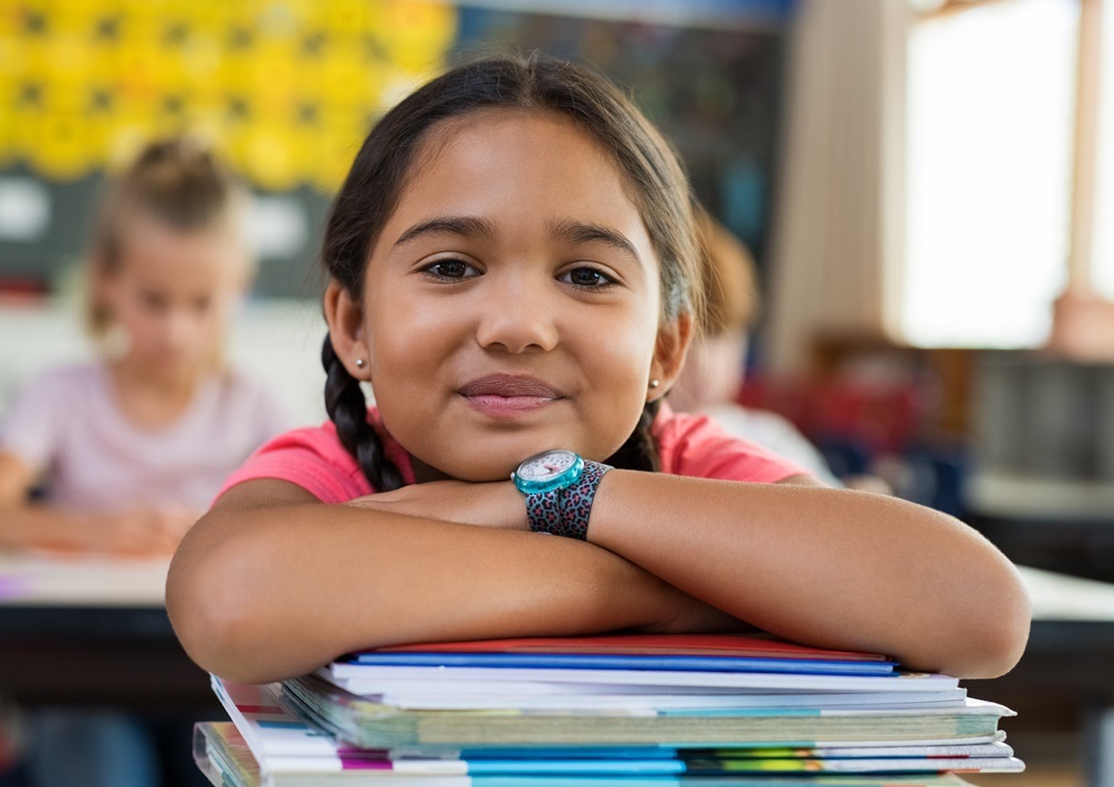 A photo of a student sitting at a desk, smiling at the camera