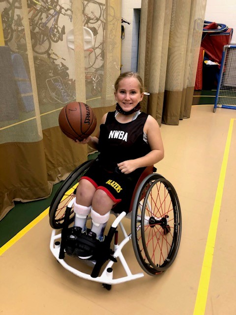 Liza, a Bennett Blazer adaptive athlete, holds a basketball on a basketball court.