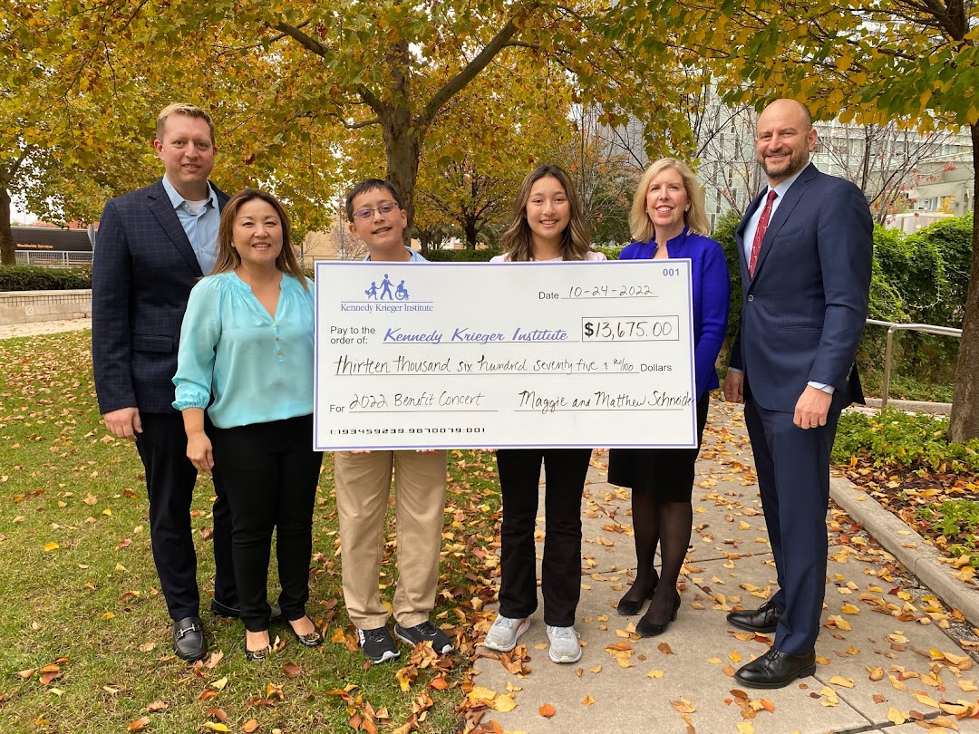 A group of people stand holding a large donation check to Kennedy Krieger Institute.