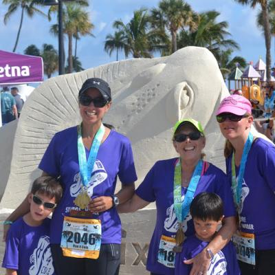 The Clark family stands together on the beach in front of a sand sculpture of a fish.