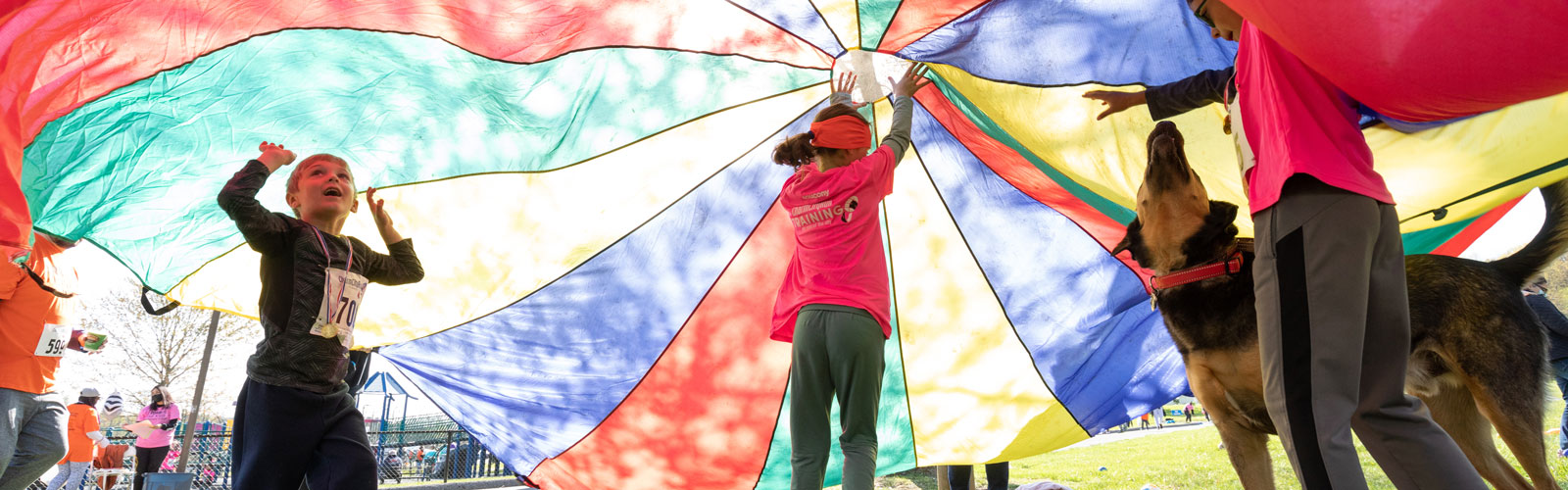 A group of children playing under a colorful parachute at ROAR 2022.