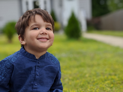 A little boy smiles while sitting in front of his house.