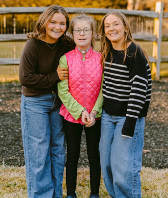 Emmy and her sisters smile while standing in the family's backyard.