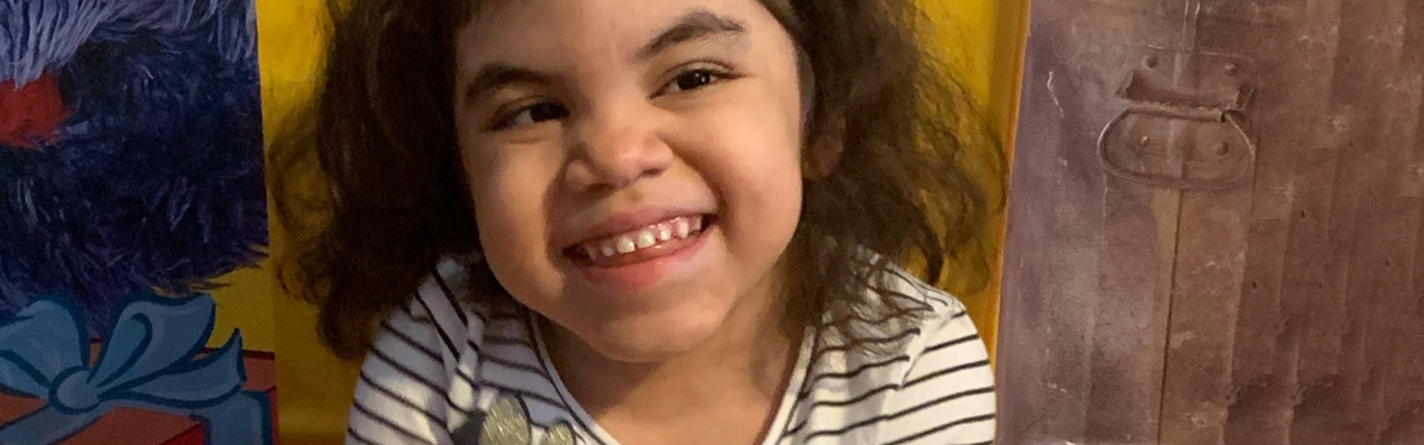 A young girl smiles while sitting in a yellow chair.