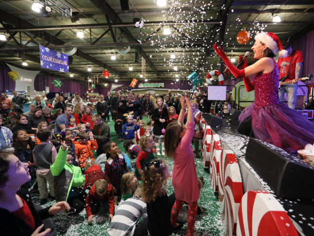 A woman stands on stage and sings before a crowd at Festival of Trees.