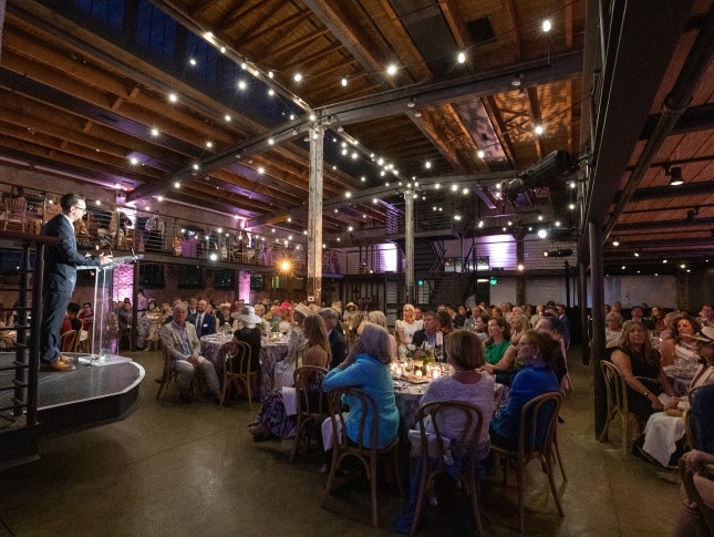 A crowd shot of Hats & Horses. The photo is taken from the back of the room, showing people seating at round banquet tables.