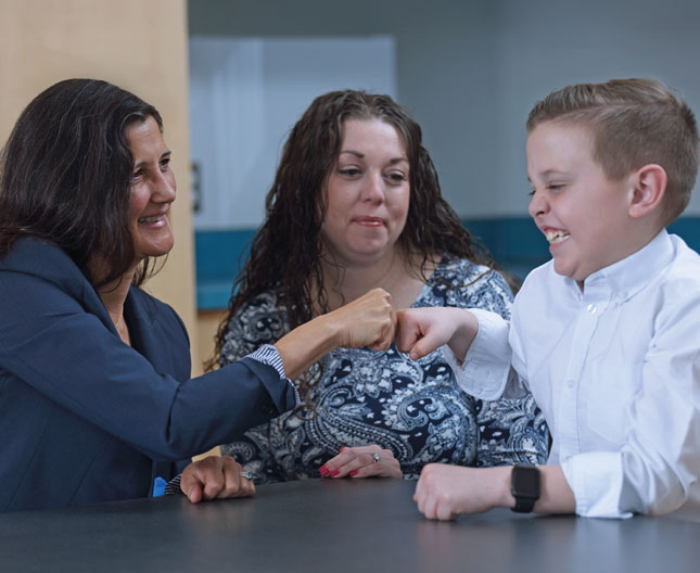 Three people smile as Dr. Vasa and a young boy share a fist bump across a table while another woman looks on.