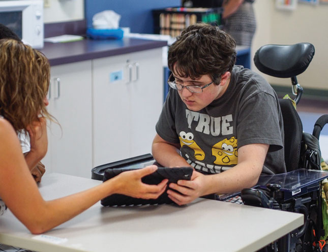 A teacher helps a student use a tablet.