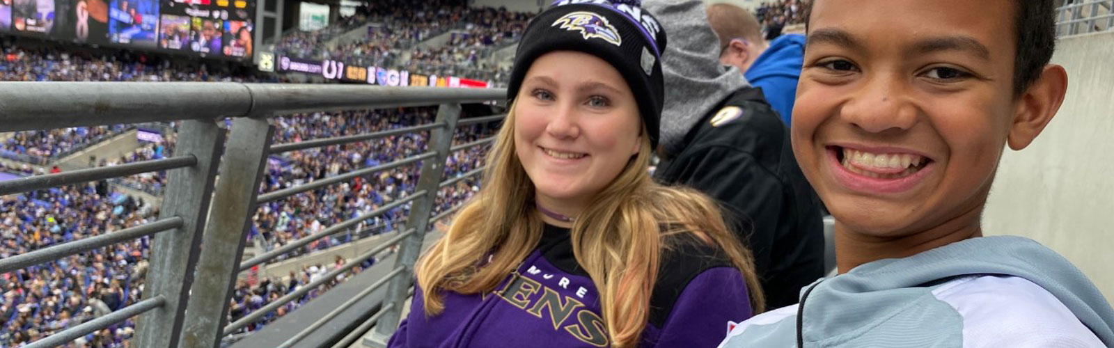 Two teenagers smile while sitting in the stands at a Baltimore Ravens game.