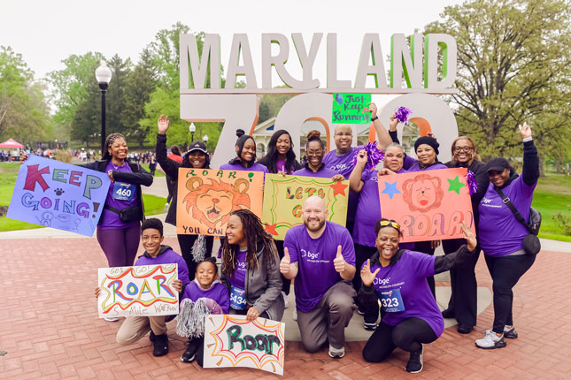 The BGE team stands poses in front of a Maryland Zoo sign while holding signs that encourage ROAR participants.