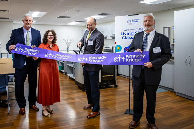Four people smile while participating in a ribbon-cutting ceremony for a living skills classroom at Kennedy Krieger's Powder Mill Campus.