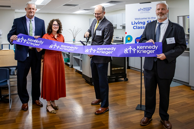 Four people smile while participating in a ribbon-cutting ceremony for a living skills classroom at Kennedy Krieger's Powder Mill Campus.