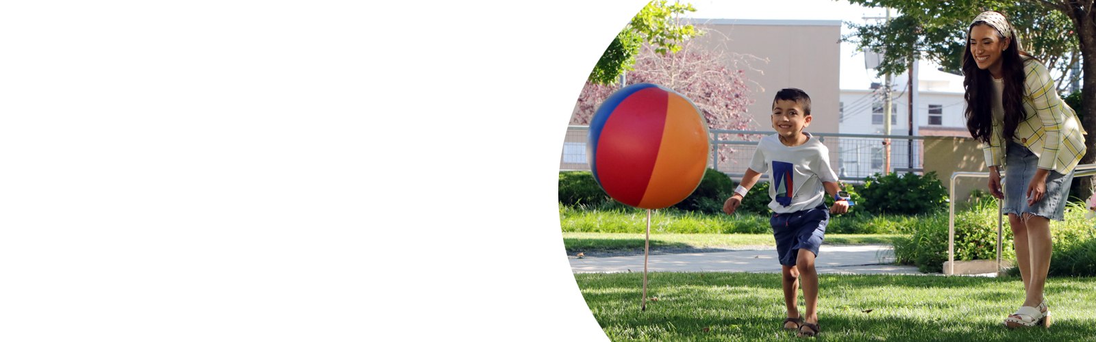 A young boy chases a beach ball in Kennedy Krieger's therapy garden as his mother stands behind him and smiles.