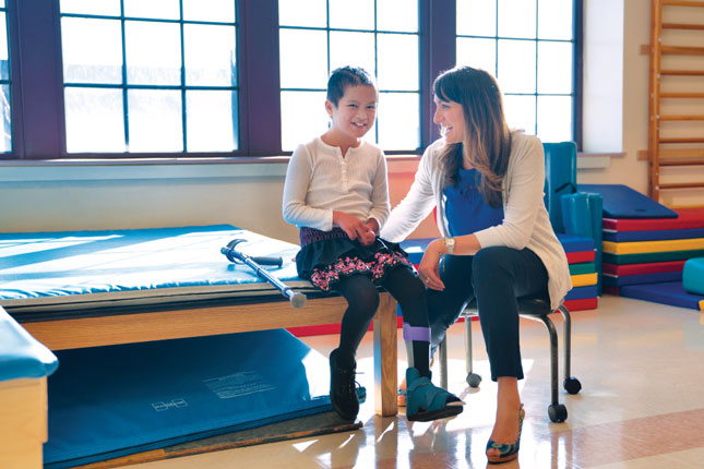 A young girl smiles while talking to a member of her care team.