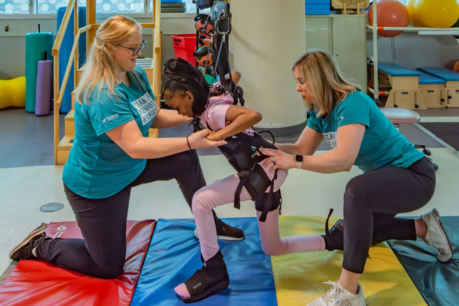 Two physical therapists assist a patient as she uses a gait device.
