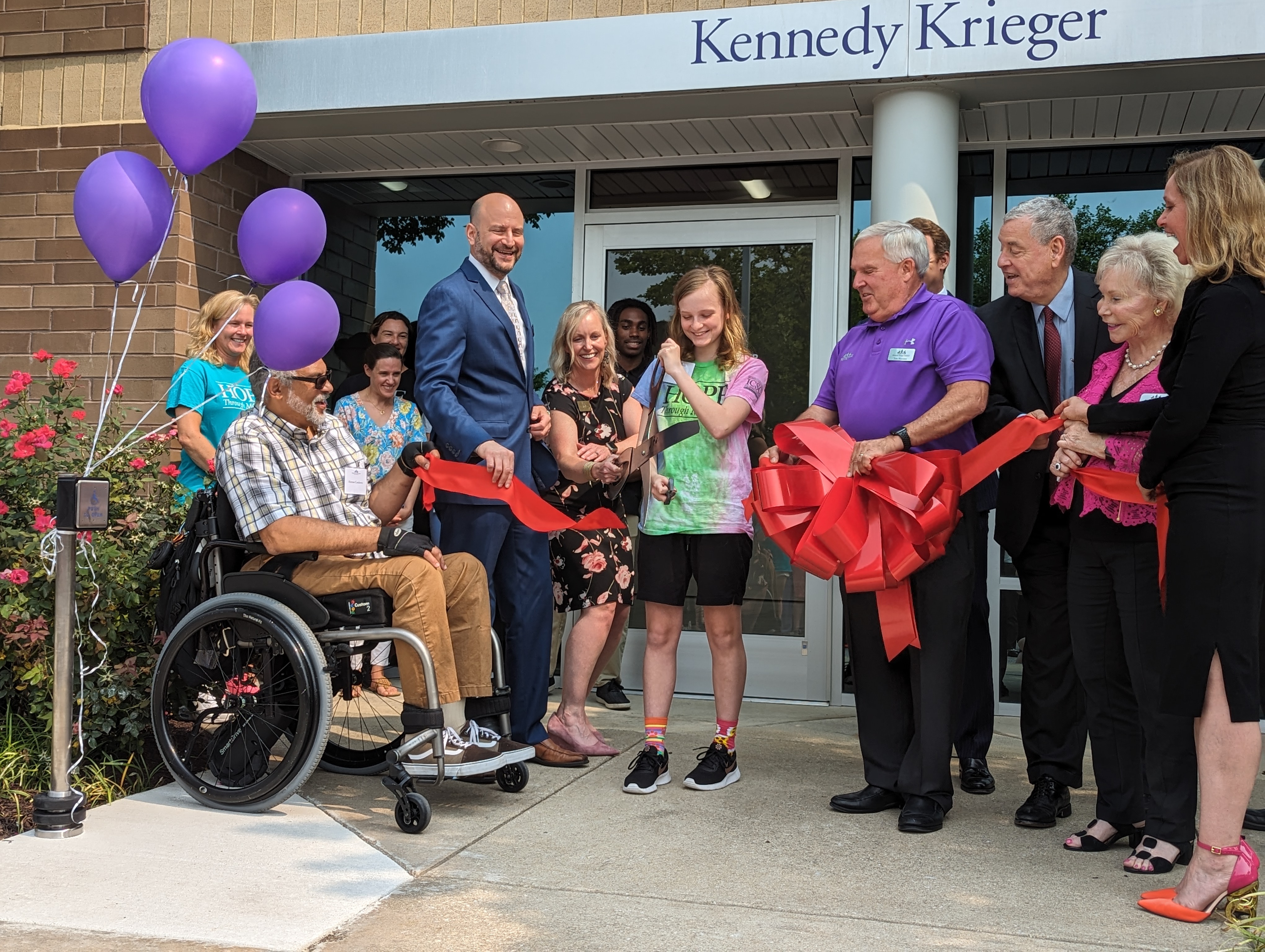 A group of people gathering around a young girl as she cuts a red ribbon to open the International Center for Spinal Cord Injury's White Marsh location.
