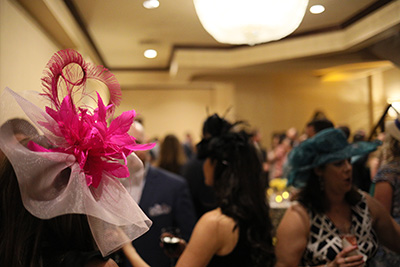 Women in a crowd wearing extremely colorful and extravagant hats.