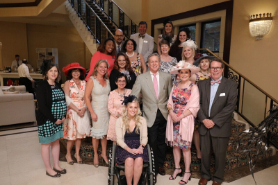 A group of guests stand together and smile for a photo, some wearing colorful hats.