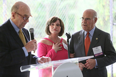 Three people stand at a podium, one holding a microphone who is presenting.