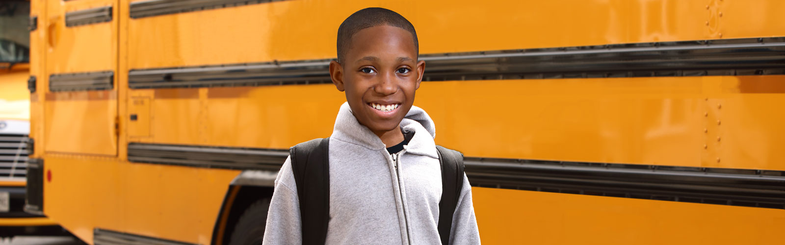 A smiling boy stands in front of a school bus. 