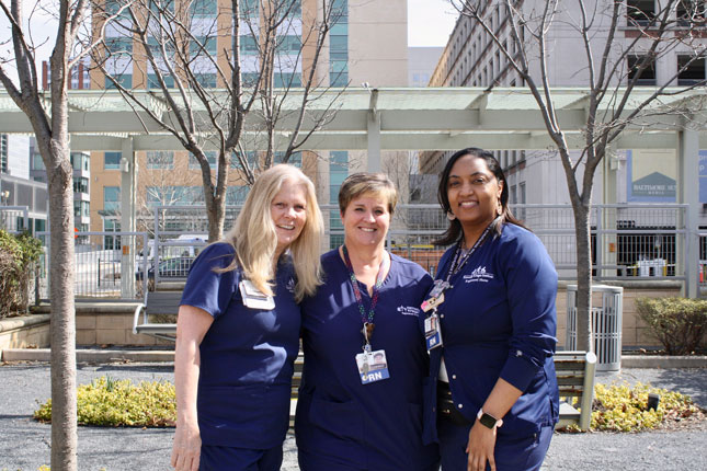 Three Kennedy Krieger nurses smile in a group photo. They are standing in Kennedy Krieger's therapy garden.