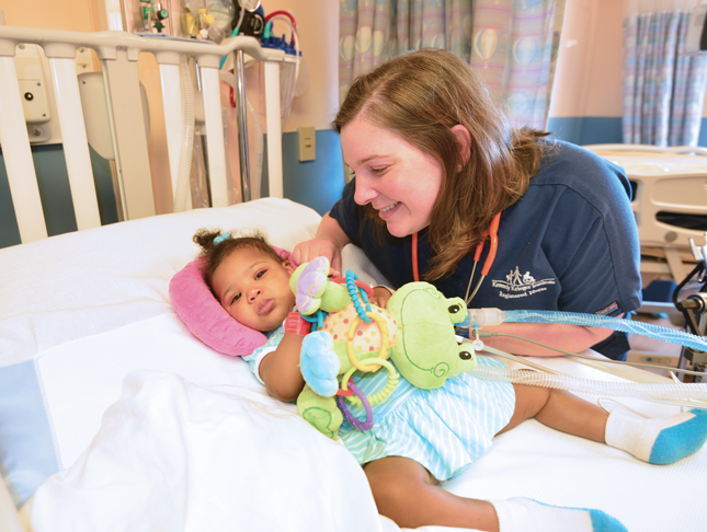 A female nurse leans over a hospital bed to tend to her patient.