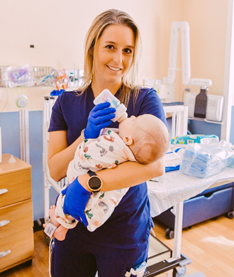 A nurse holds a baby while feeding it from a bottle.