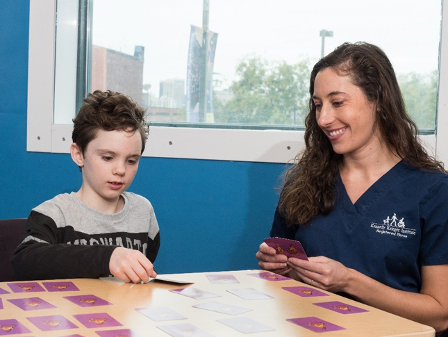 A nurse and a boy sit at a table and play a card game together.