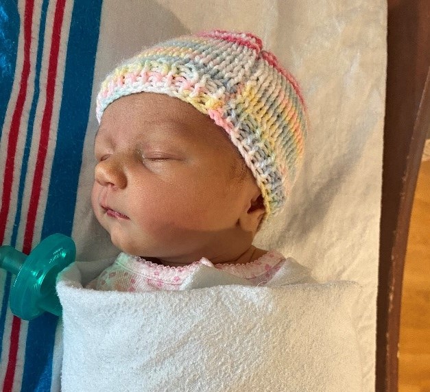 A newborn baby girl sleeps under a white blanket.