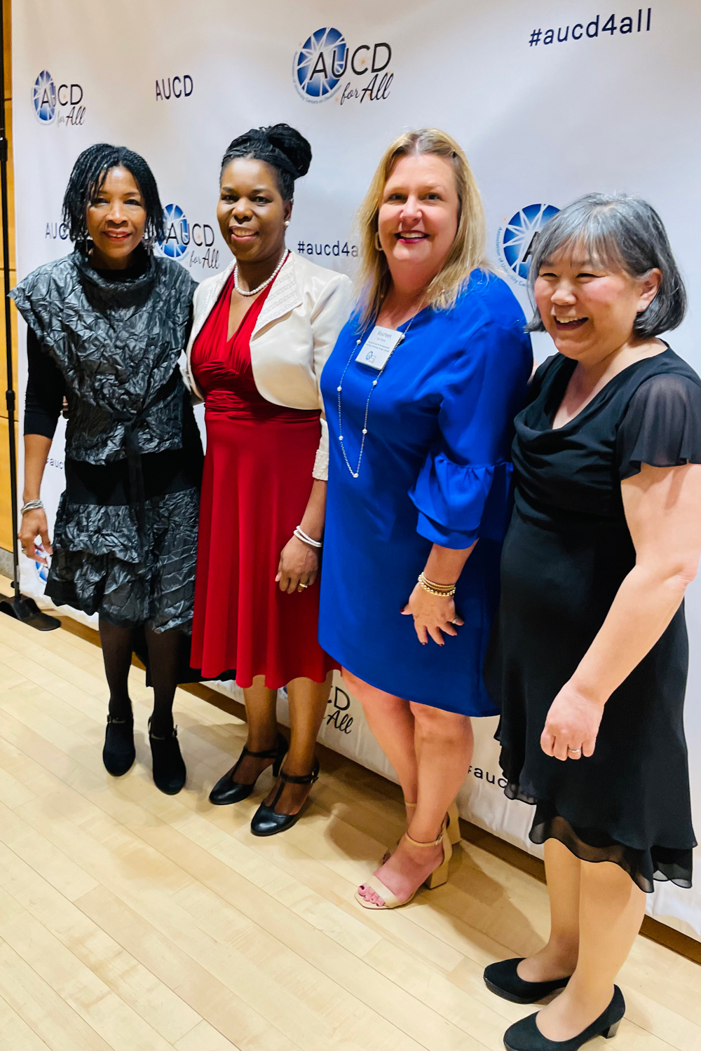 Four women stand in front of an AUCD branded banner at the Association of University Centers on Disabilities (AUCD) Gala.