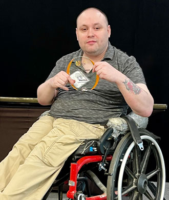 Mat RIce sits in his mobility device and holds the Catalyst Award at The Arc Maryland’s Statewide Convention and Awards Banquet.