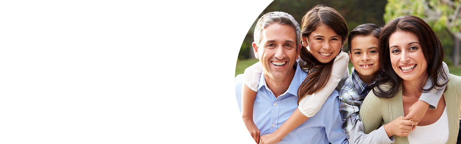 A father, mother, daughter and son smile in a family portrait that is taken outside.