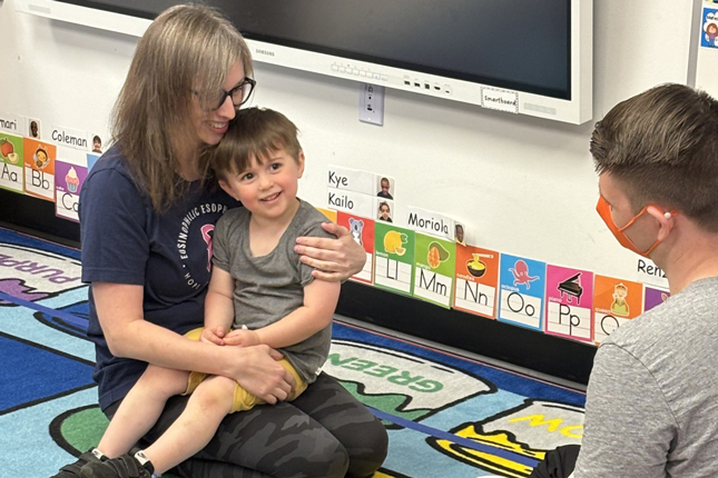 A little boy and his mom smile while sitting in a classroom with an EDEC staff member.