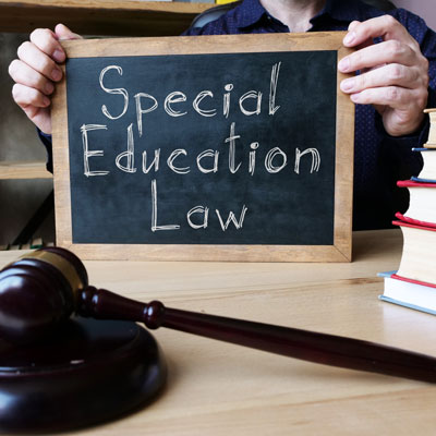 Small chalkboard with text Special Education Law. An unseen person is holding the chalkboard, with the bottom of the board resting on a table with books and a gavel. 