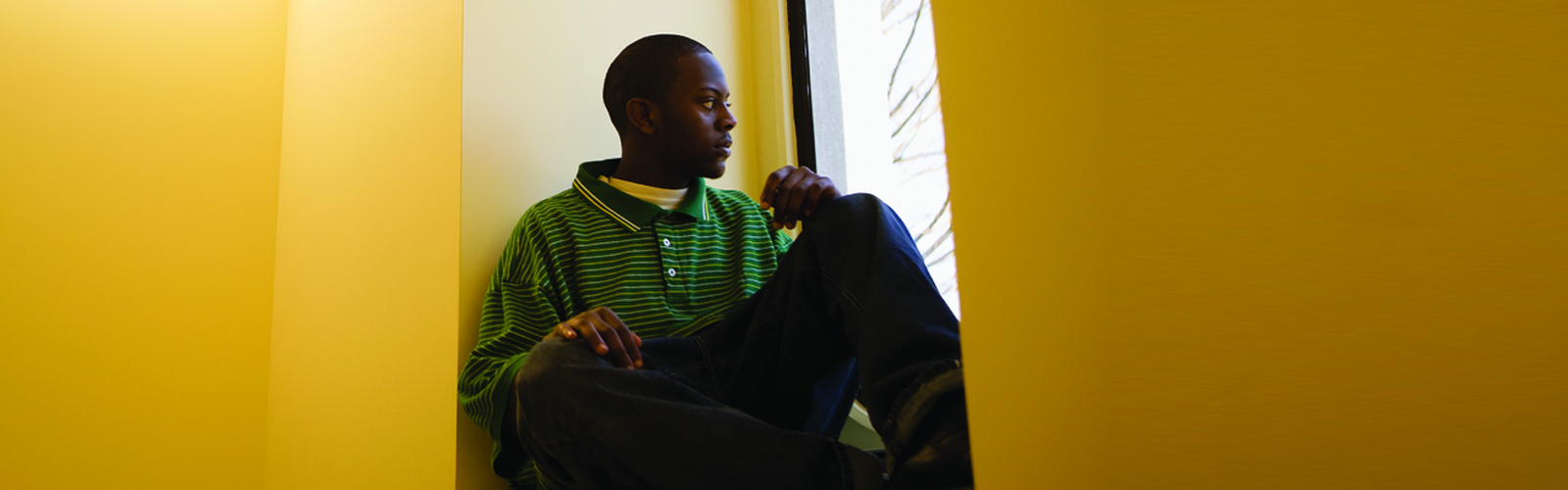 A man looking out of a window in a yellow room.