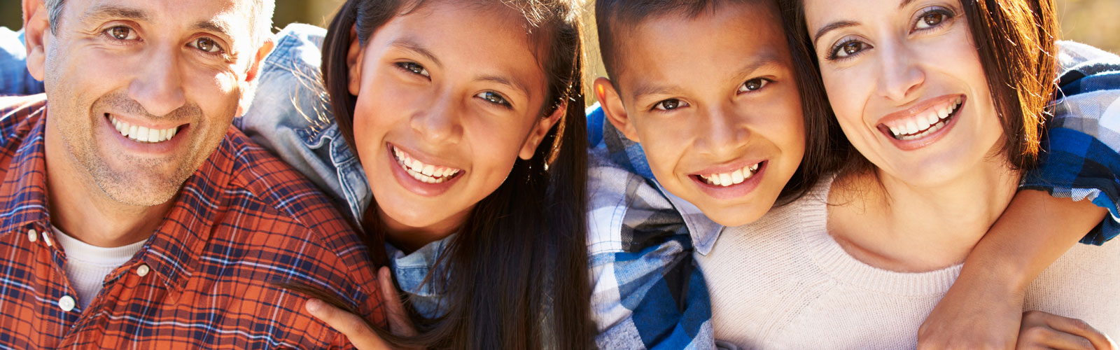 A father, daughter, son and mother smile in an outdoor portrait.