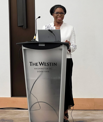 Dr. Mirian Ofonedu smiles while standing behind a podium.