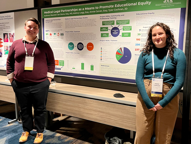 Tyler Cochran and Annie Carver stand in front of their poster presentation and smile.