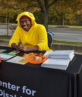 Chris Mason-Hale sits behind MCDD's table at PACT and smiles.